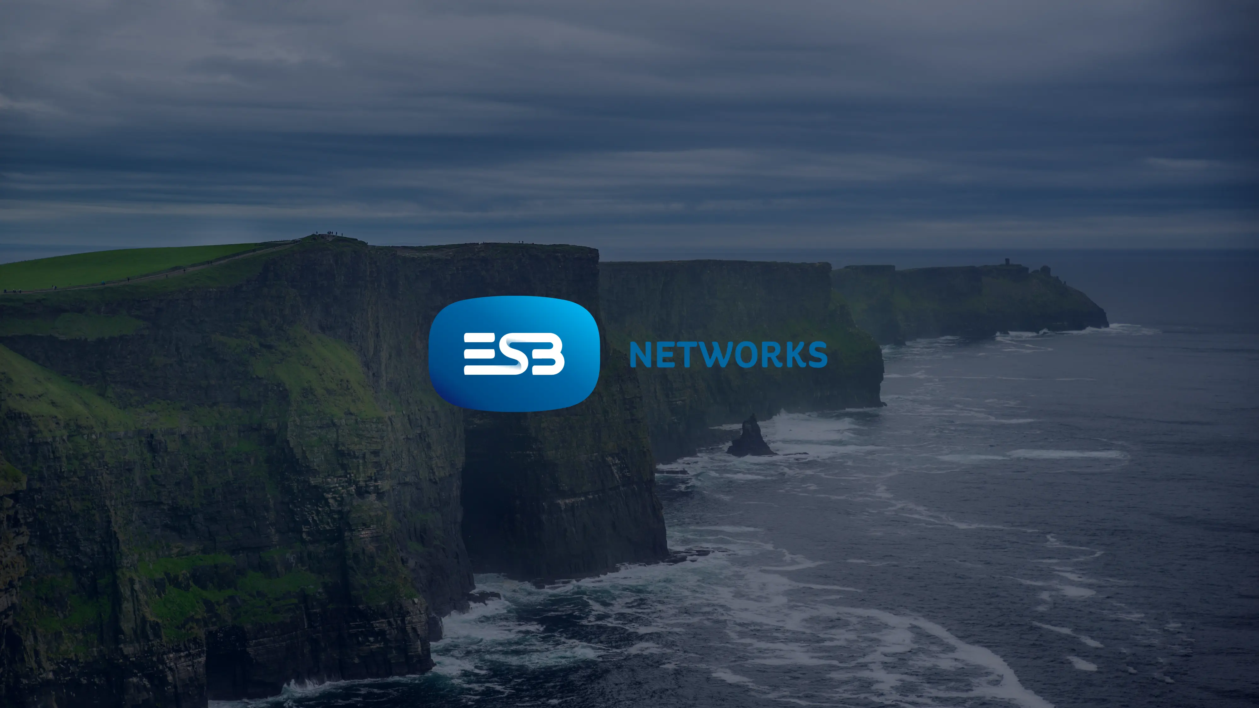 Steep coastal cliffs with waves and cloudy sky with the ESB Networks logo centered.