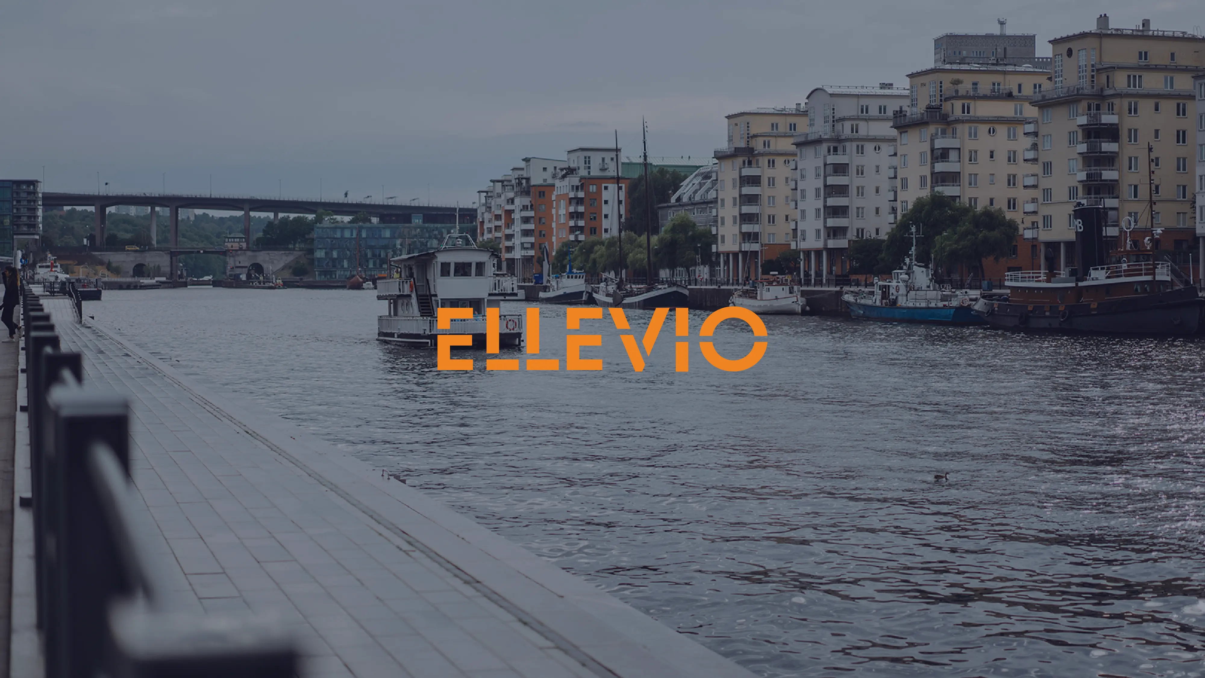 Riverfront cityscape with boats, apartment buildings, a walkway, a bridge, and ELLEVIO text.